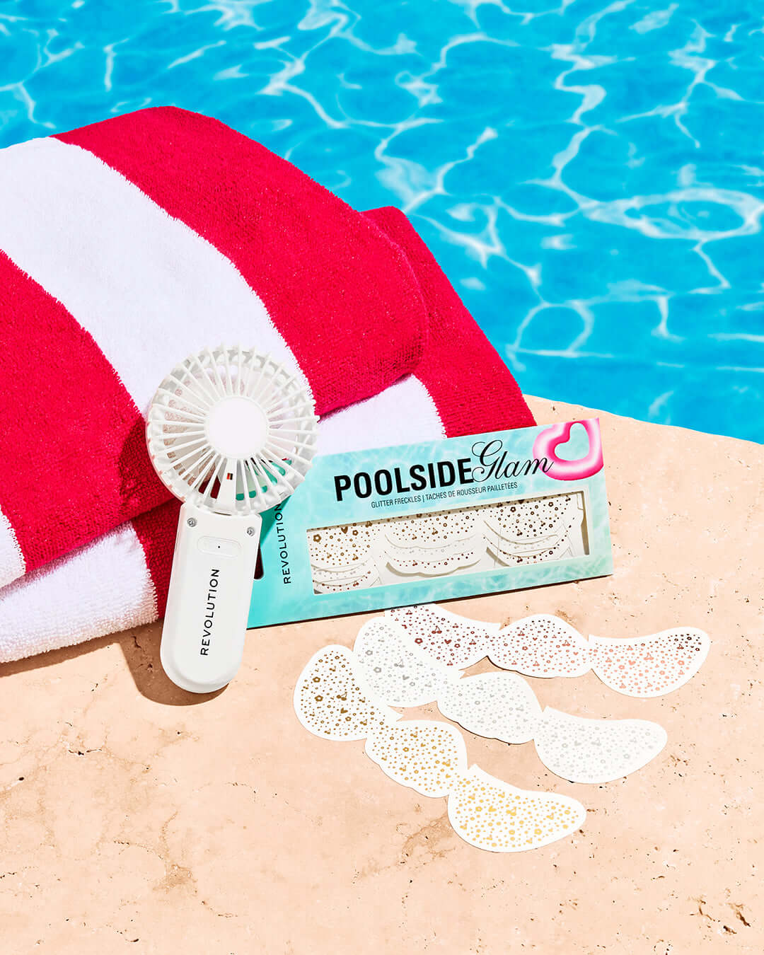 Revolution Poolside Hand Held Electric Fan White beside pool towel and glitter freckle stickers.
