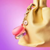 Revolution Sparkly Lip & Cheek Jelly in a pink pot with charm, attached to a yellow bag, against a colorful background.