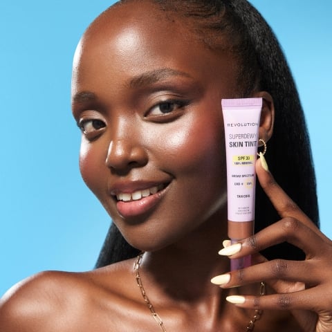 woman holding Revolution's Skin Tint on a blue background